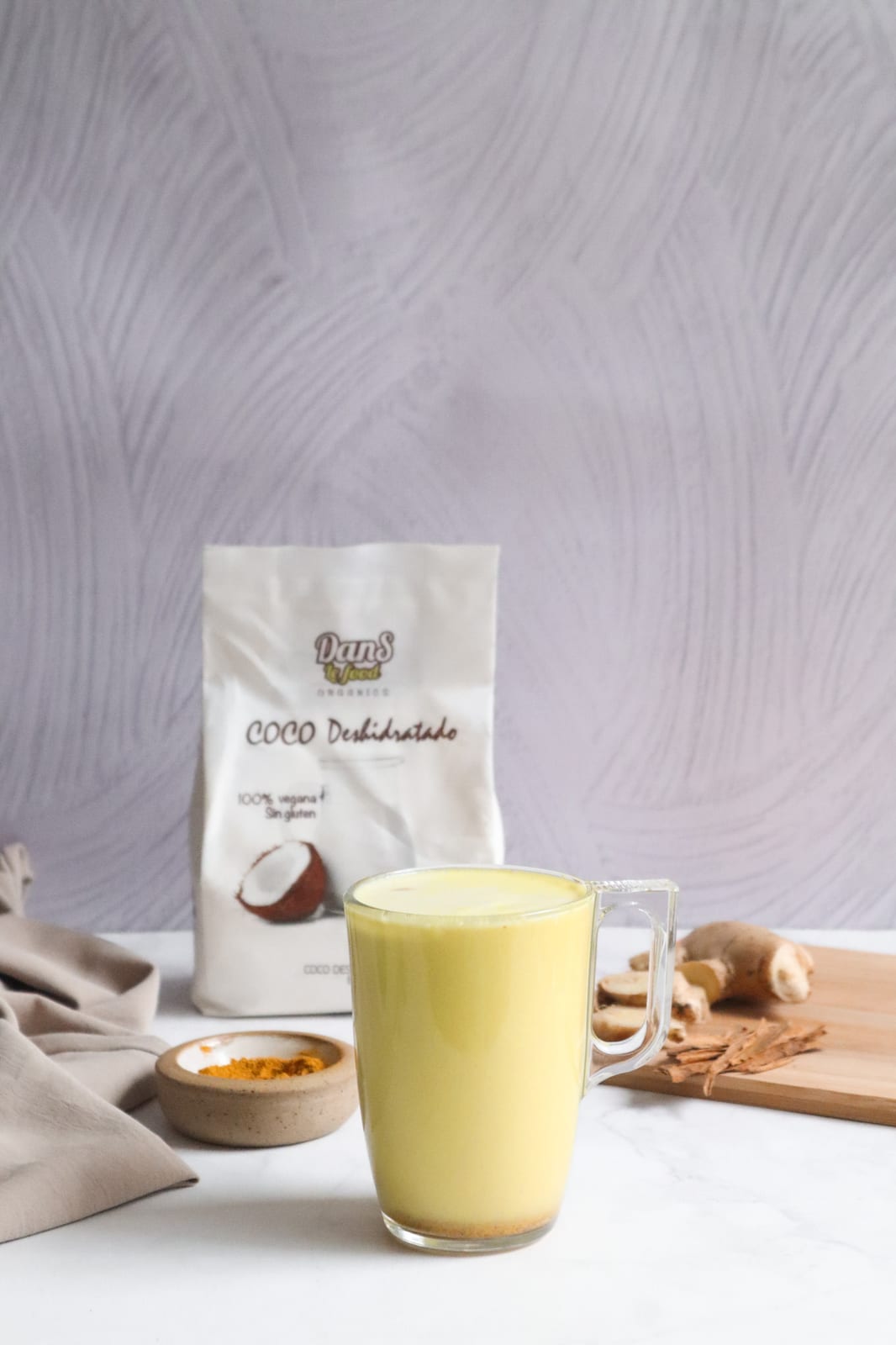Leche dorada con leche de coco servida en taza de vidrio junto a cúrcuma en polvo