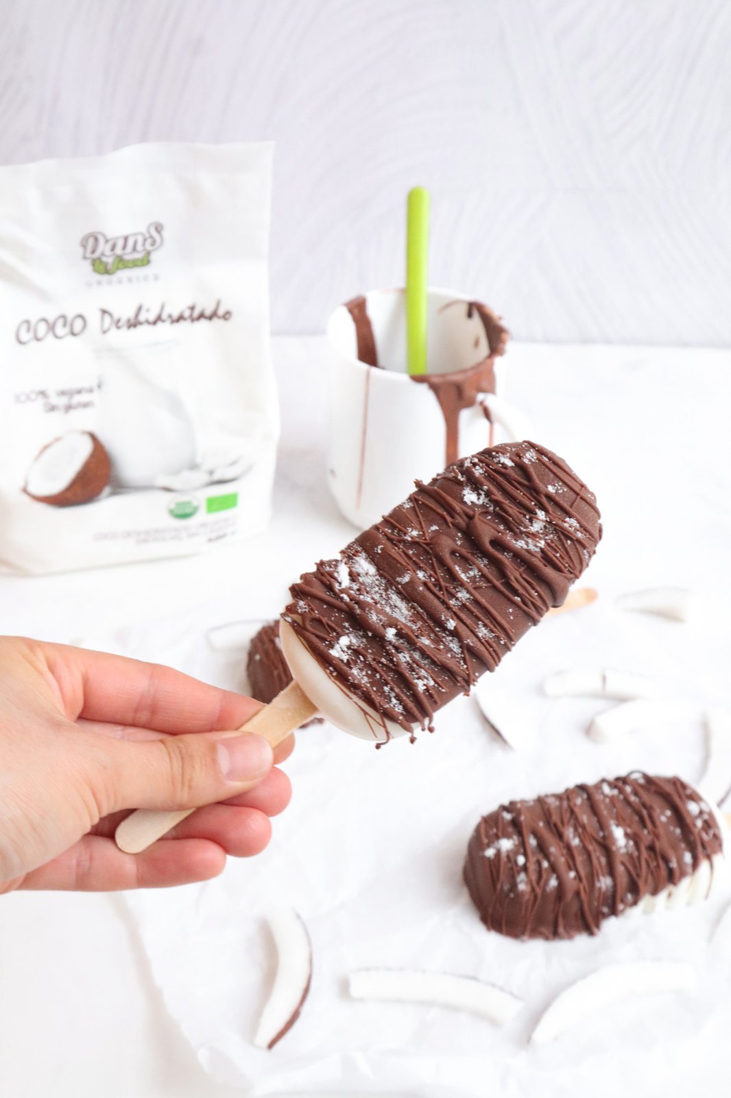 Paletas heladas de coco bañadas en chocolate negro y decoradas con coco rallado